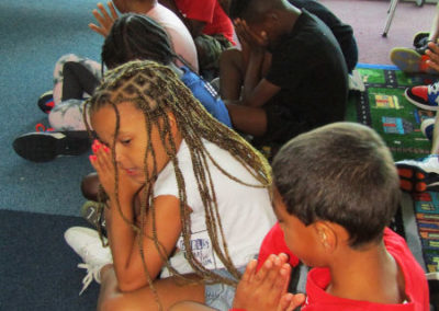 Seven children sit on the floor praying with their hands folded