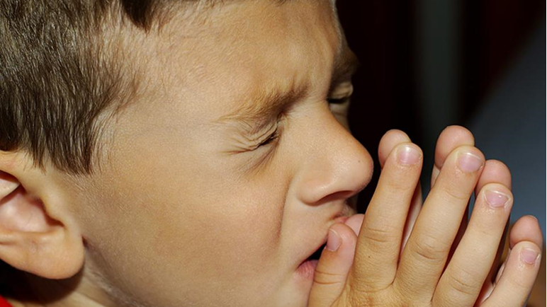 A boy prays with his eyes closed and hands folded